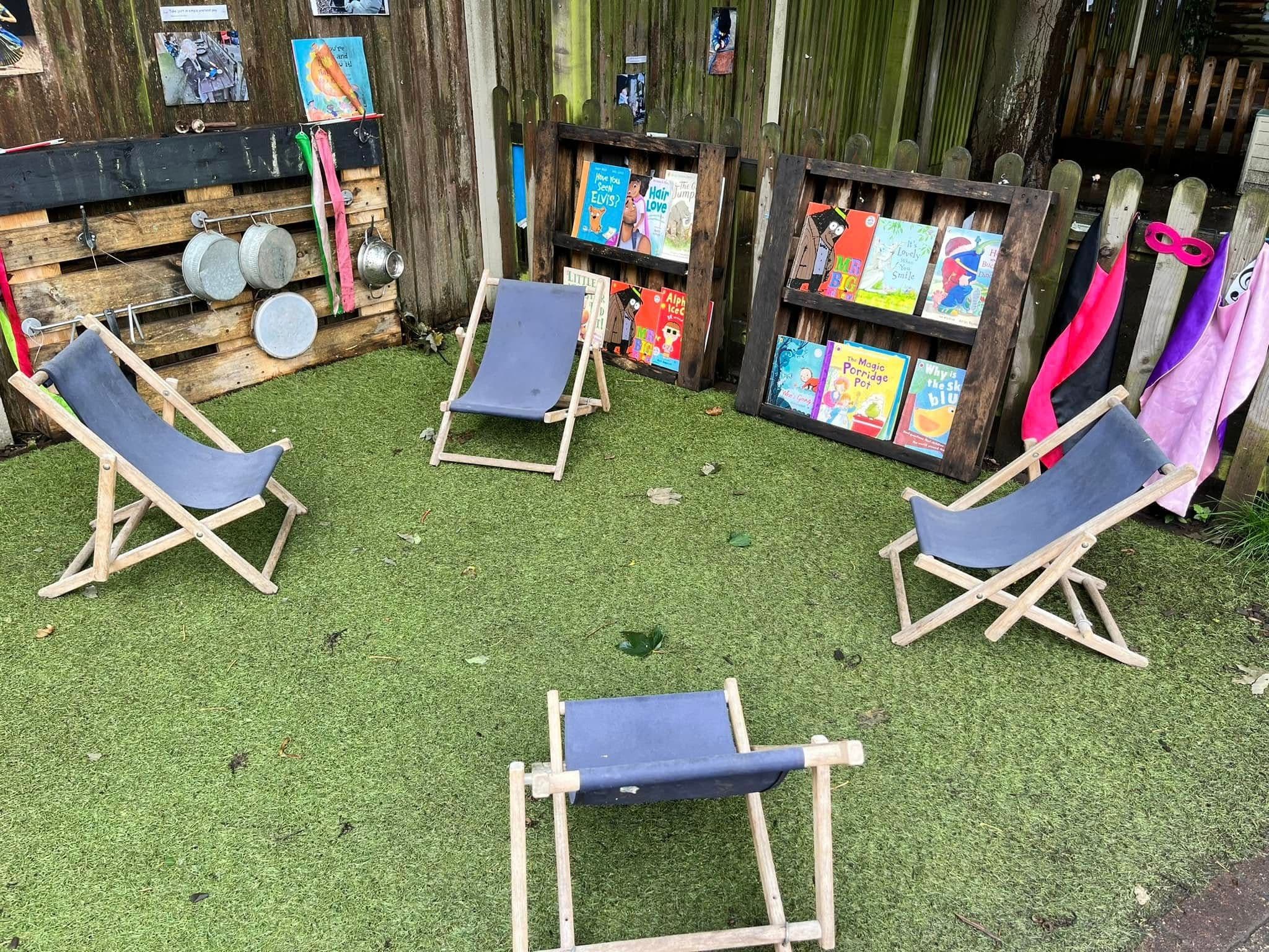 An outdoor book corner with folding deckchairs and picture books propped along a fence.