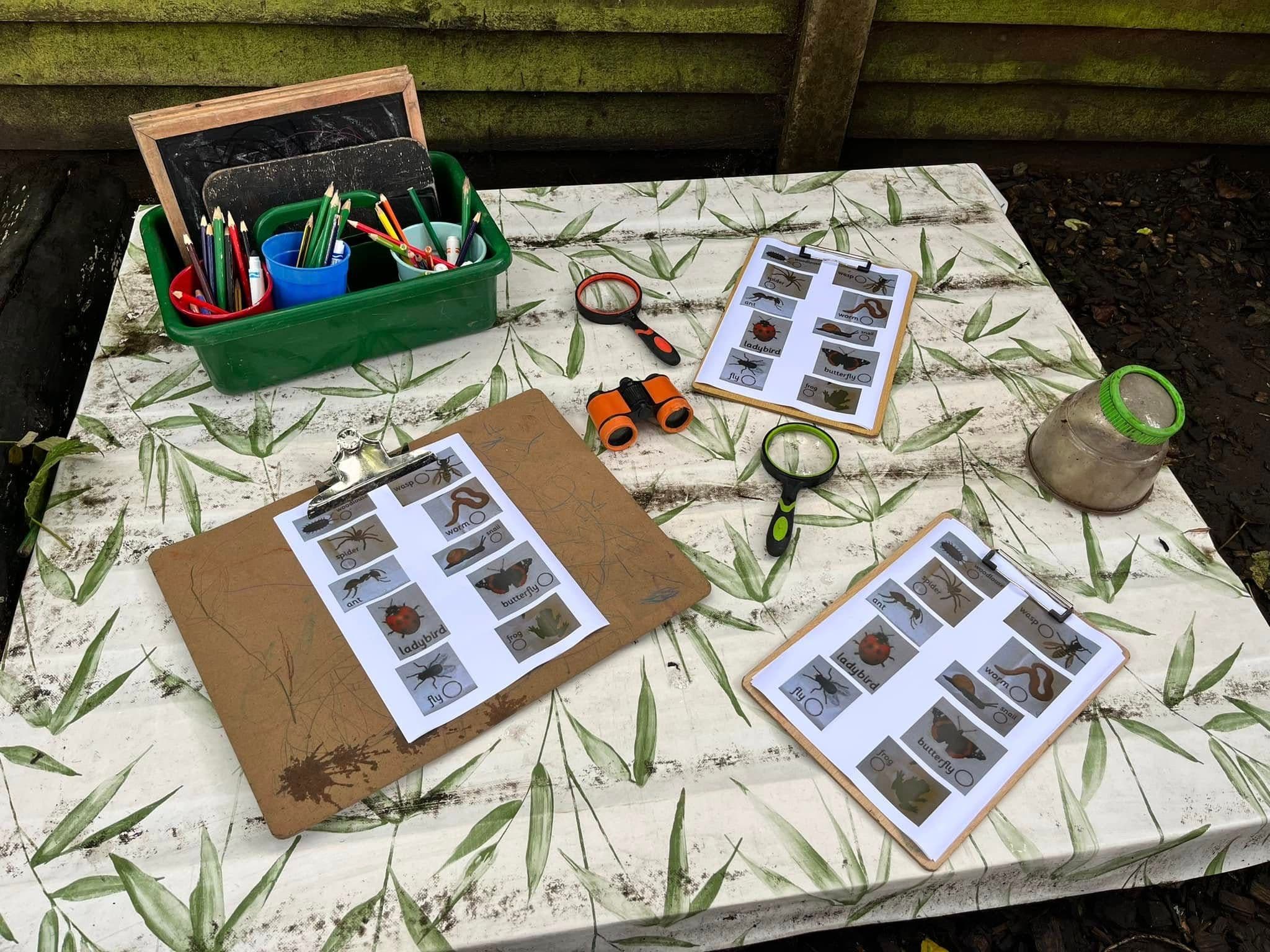 An outdoor nature table with clipboards, spotting sheets and magnifying glasses for a bug hunt.