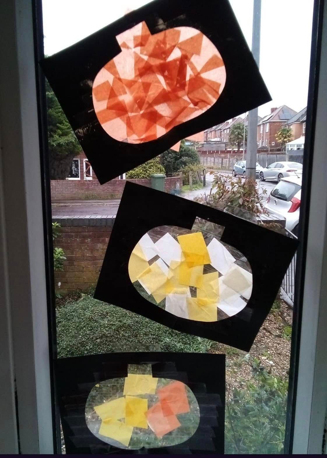 Autumn pumpkin sun-catchers made from orange and yellow tissue paper displayed on a window.