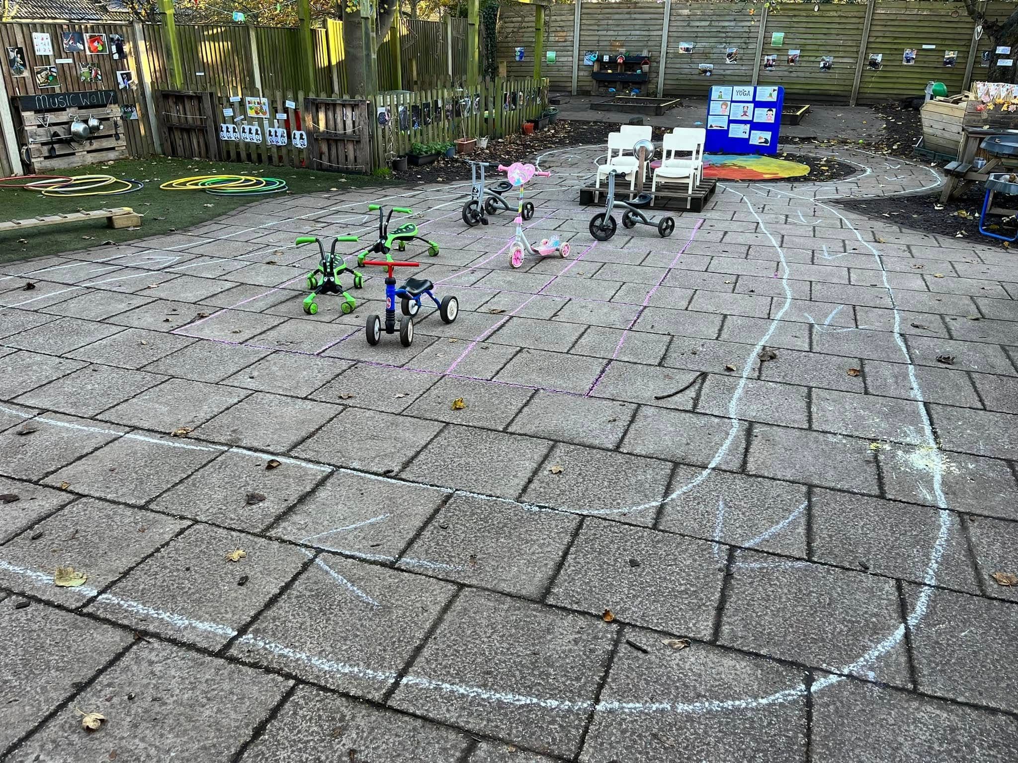 A paved outdoor play yard with children's trikes and chalk-drawn roads.