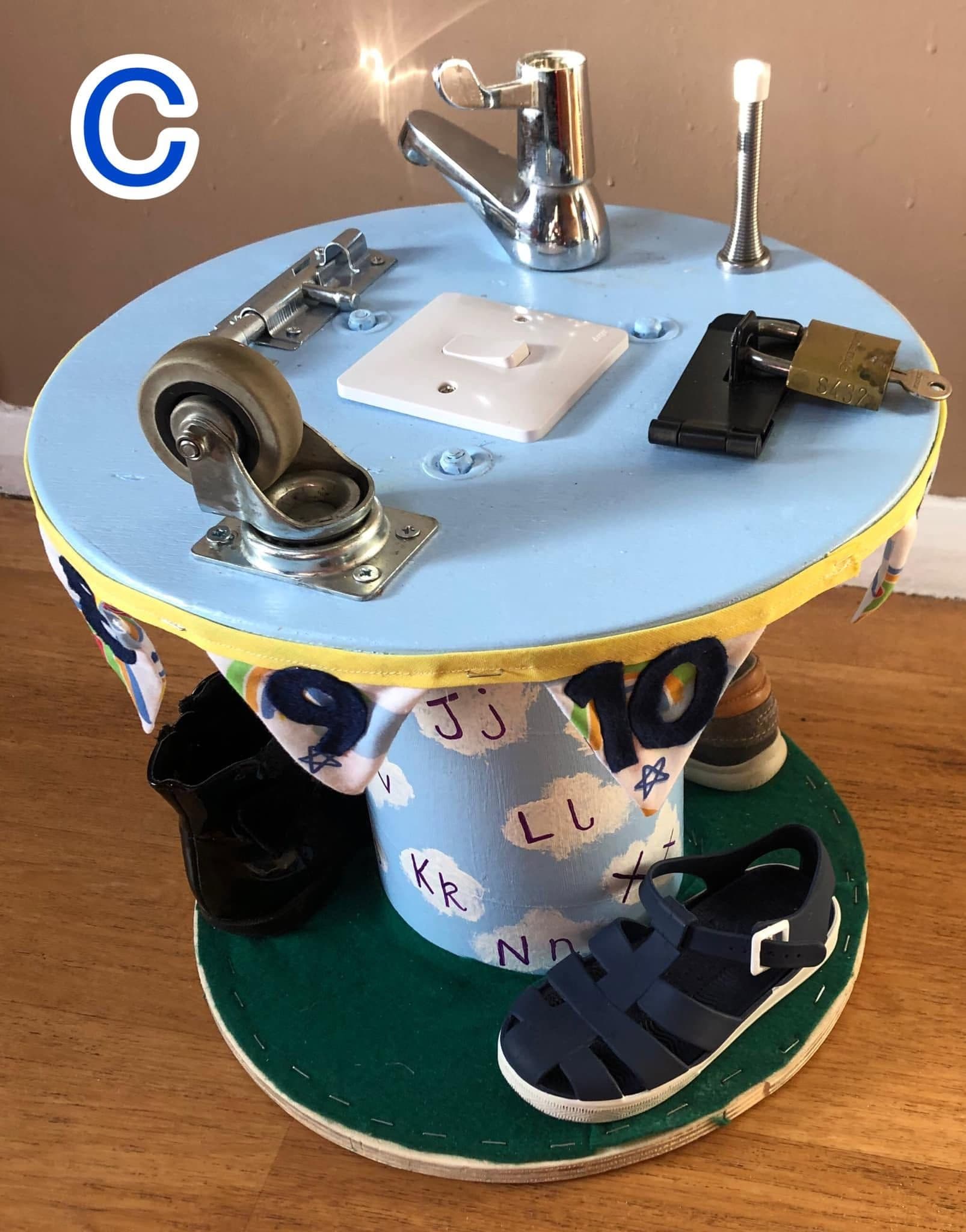 A home-made wooden sensory board fitted with taps, padlocks, a light switch and a caster wheel.