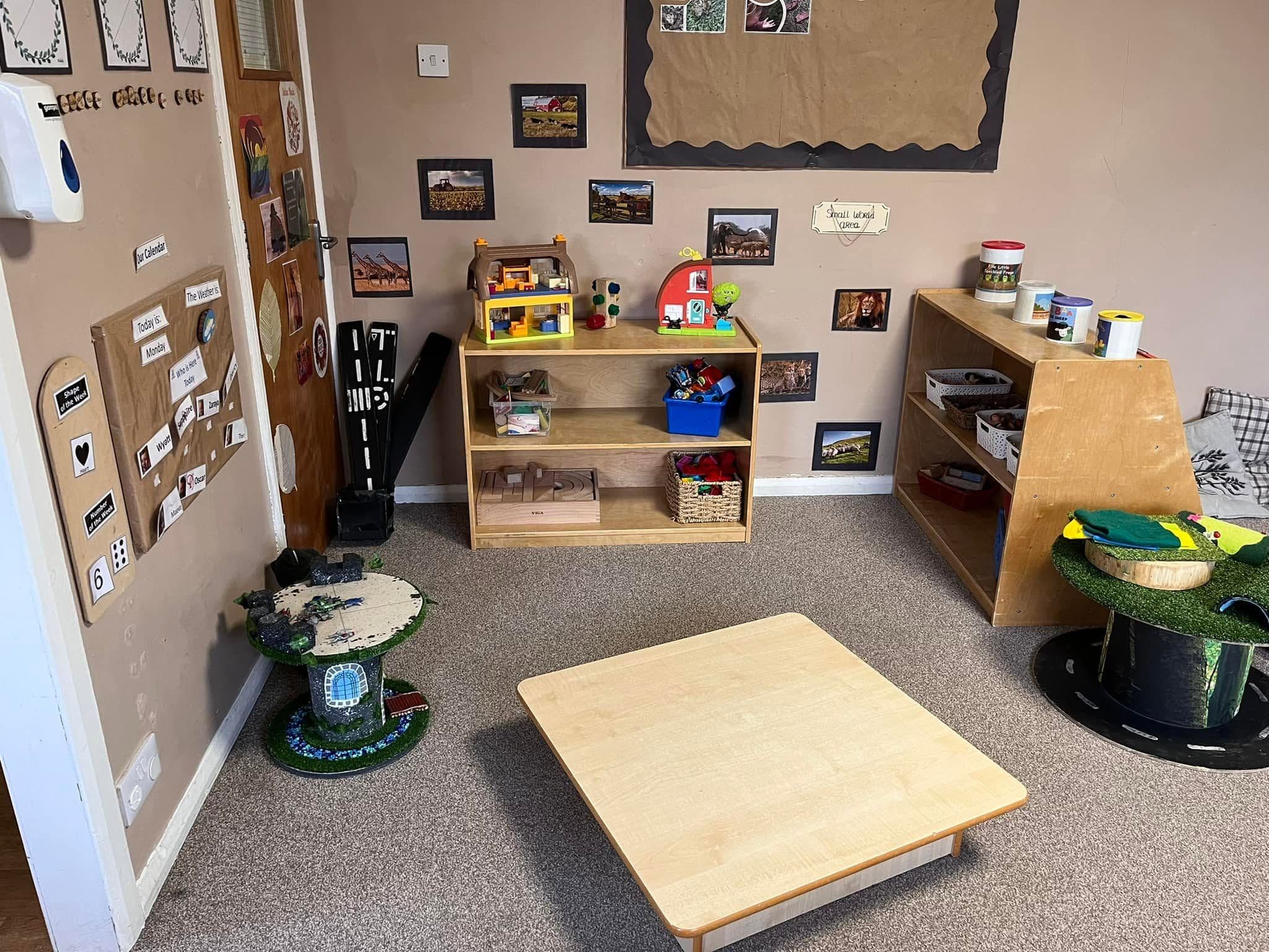 A nursery playroom with wooden storage shelves, toys and a low wooden activity table.